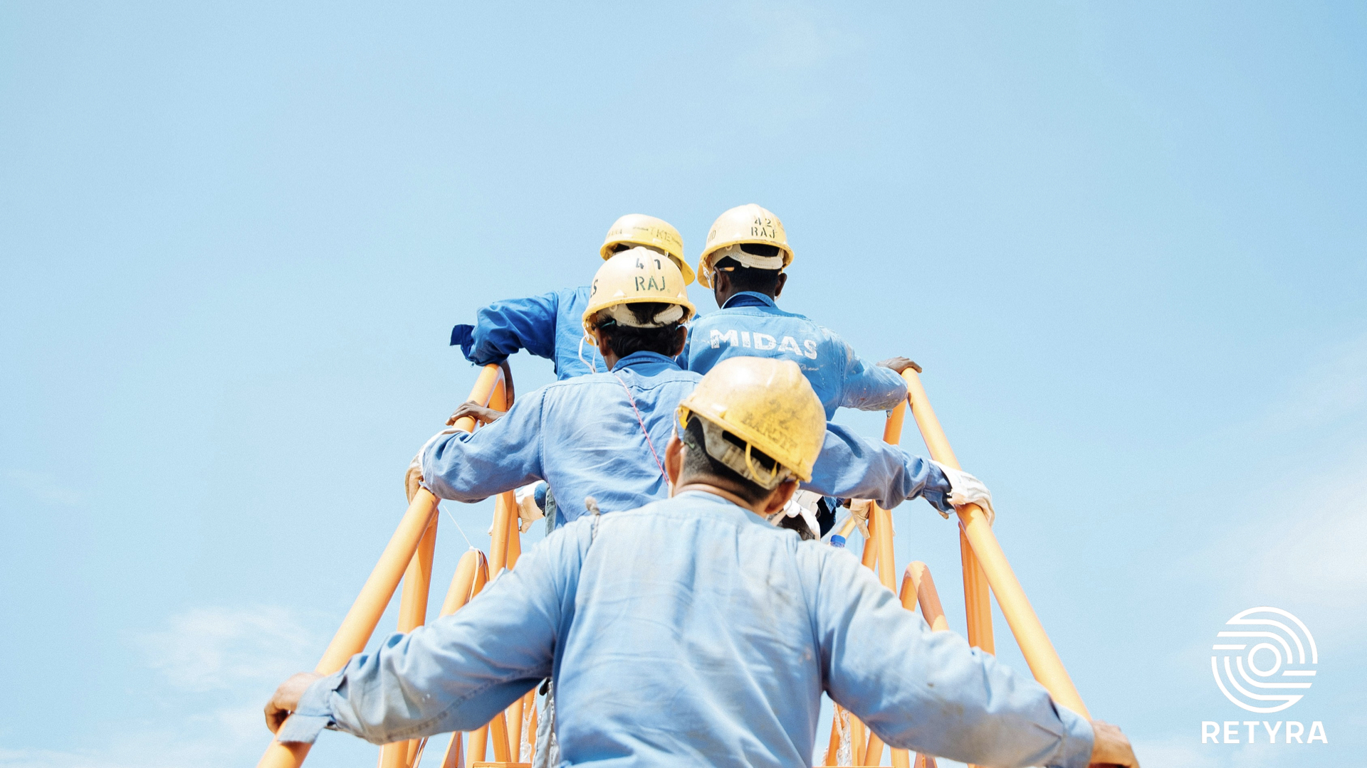 Industrial workers in blue uniforms and yellow hard hats climbing a stairway